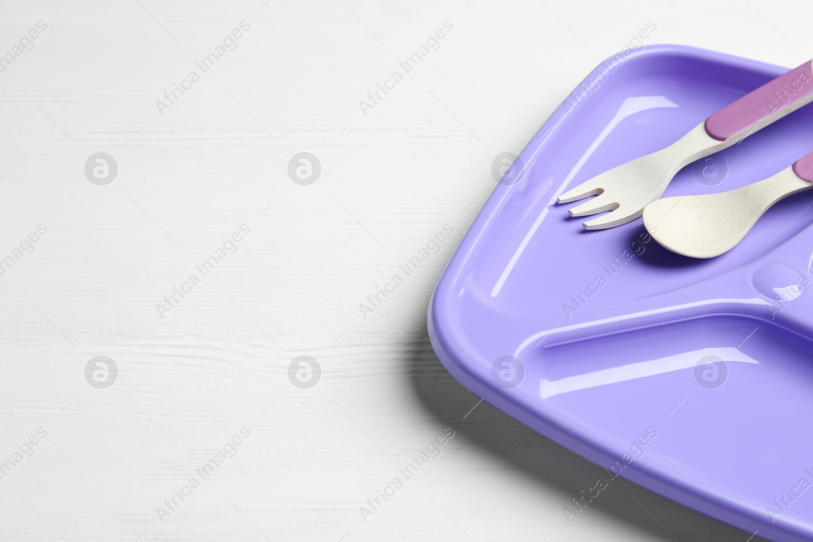 Photo of Section plate with fork and spoon on white wooden table, space for text. Serving baby food