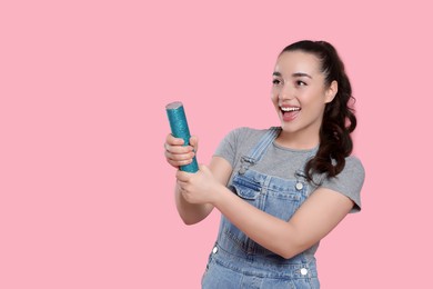Photo of Young woman blowing up party popper on pink background, space for text