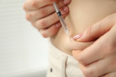 Diabetes. Woman making insulin injection into her belly indoors, closeup