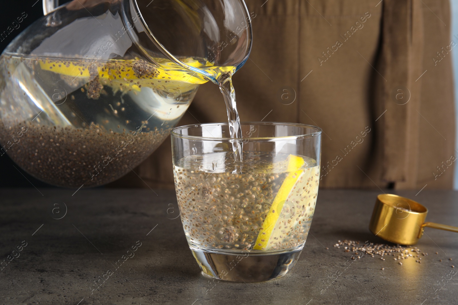 Photo of Pouring water with chia seeds and lemon into glass at table, closeup