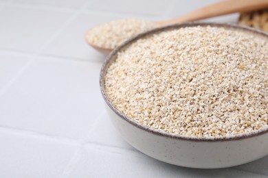 Photo of Raw barley groats in bowl on light tiled table, closeup. Space for text