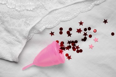 Photo of Woman's panties and menstrual cup with red confetti on white fabric, flat lay