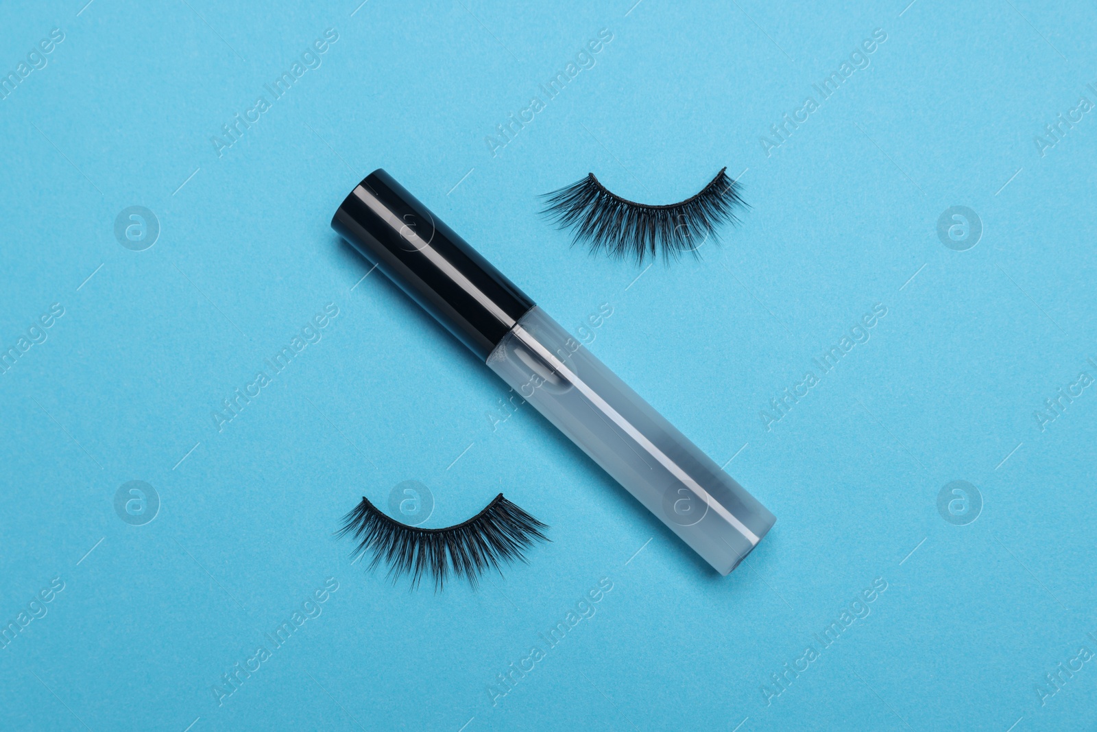 Photo of False eyelashes and tube of oil on light blue background, flat lay