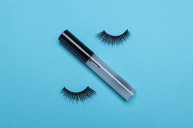 False eyelashes and tube of oil on light blue background, flat lay