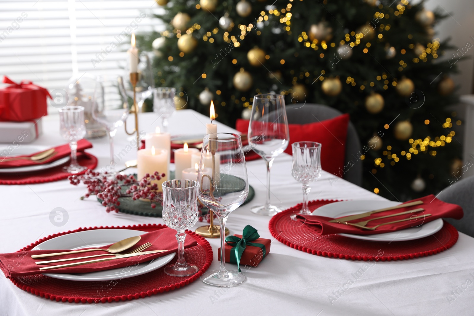 Photo of Christmas table setting with burning candles, gift box and dishware indoors