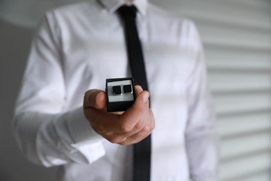 Man holding box with stylish cufflinks on blurred background, closeup