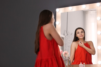 Photo of Young beautiful woman applying makeup near mirror