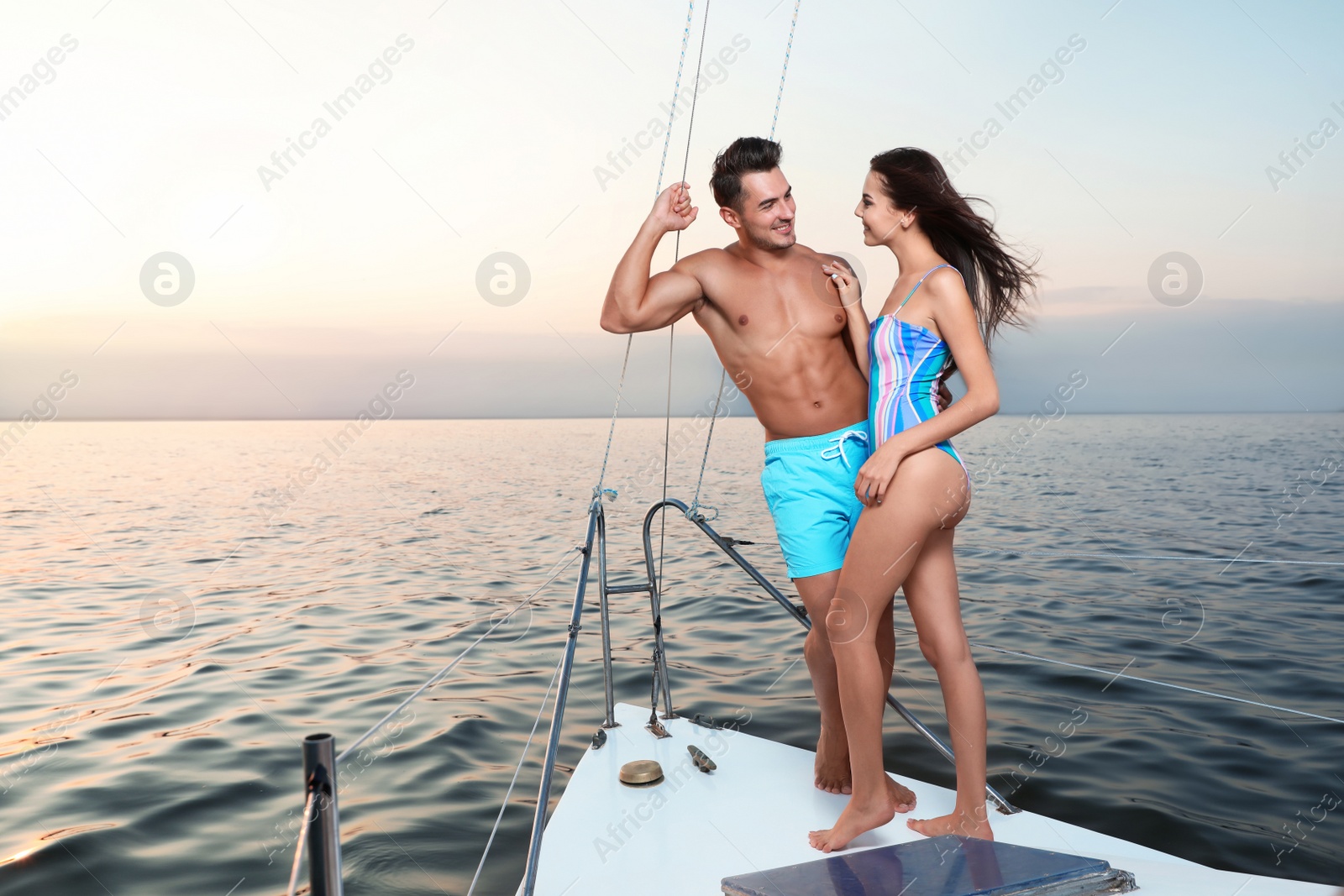 Photo of Young man and his beautiful girlfriend in bikini on yacht. Happy couple during sea trip