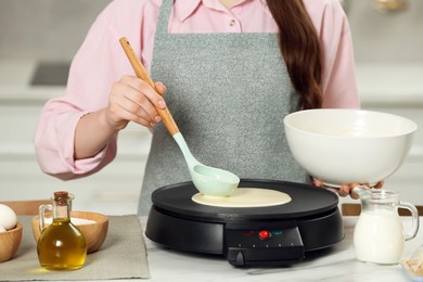 Woman cooking delicious crepe on electric maker at white marble table in kitchen, closeup