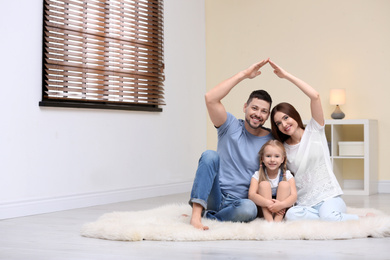 Happy family forming house roof with their hands at home. Insurance concept