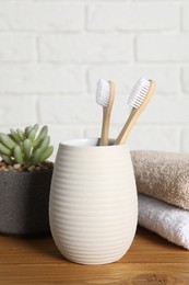 Photo of Bamboo toothbrushes in holder, houseplant and towels on wooden table
