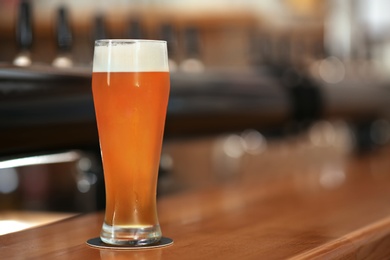 Photo of Glass of cold tasty beer on bar counter, space for text