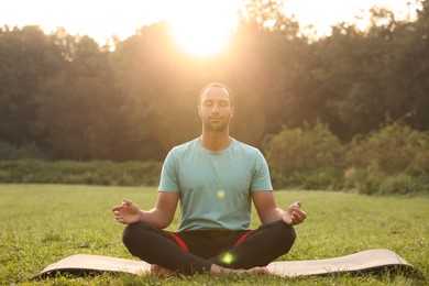 Photo of Man practicing yoga on mat outdoors. Lotus pose