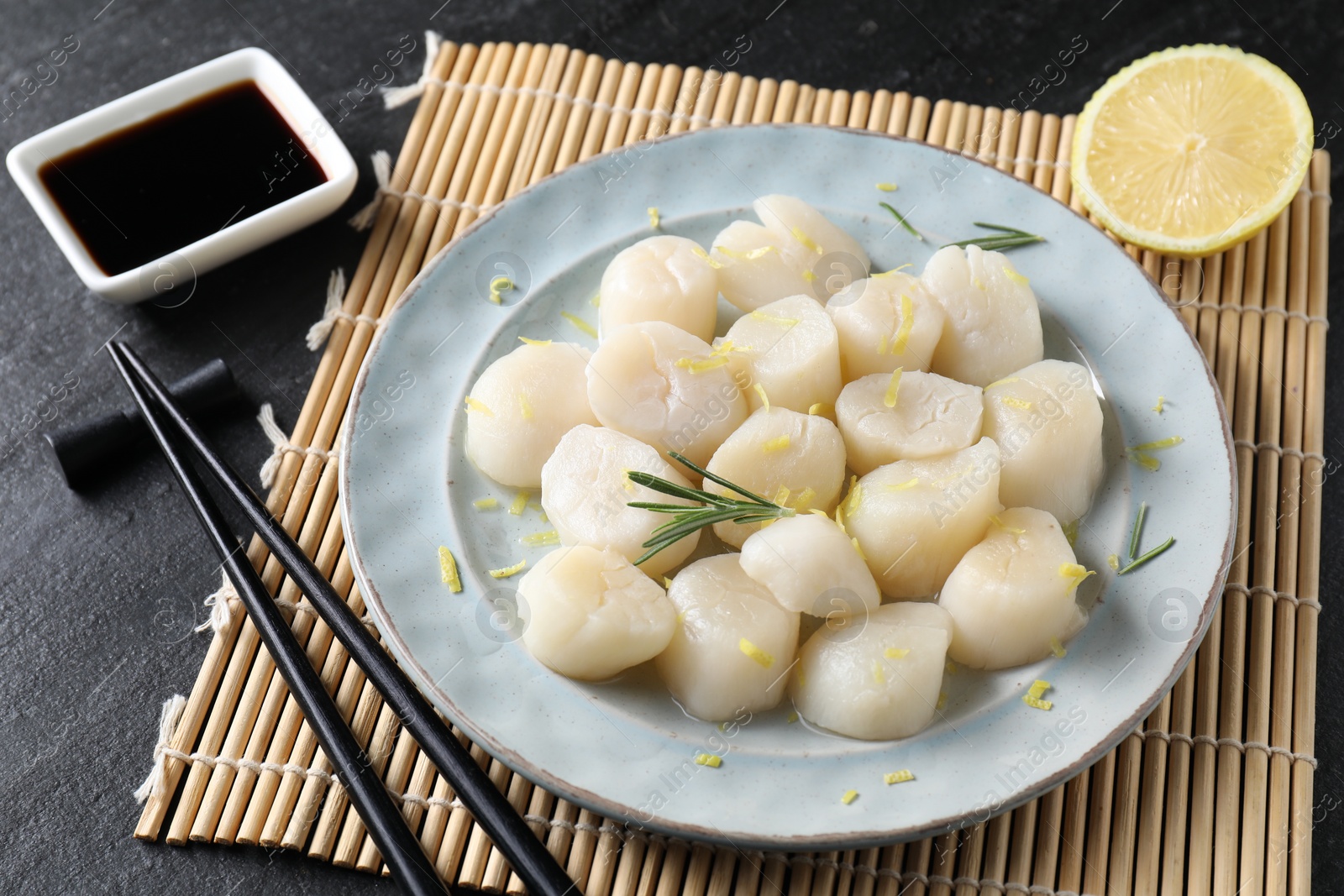 Photo of Raw scallops with lemon, rosemary and soy sauce on dark textured table, closeup