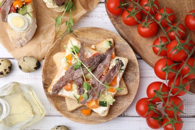 Photo of Delicious toasts with anchovies, cream cheese, bell peppers and cucumbers on white wooden table, flat lay