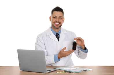 Photo of Professional pharmacist with syrup and laptop at table against white background