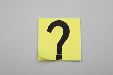 Sticky note with question mark on light grey background, top view
