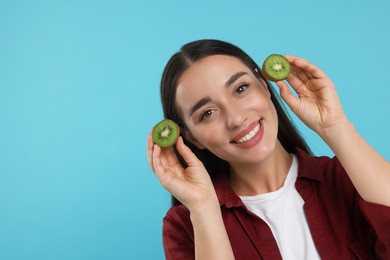 Photo of Woman holding halves of kiwi on light blue background, space for text