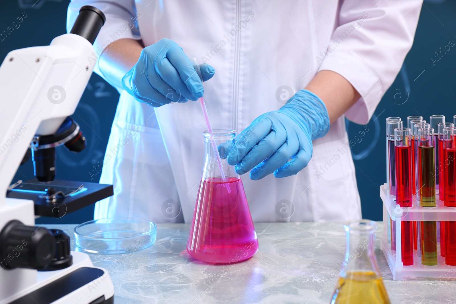 Photo of Scientist taking sample of liquid with dropper at table, closeup. Chemistry glassware