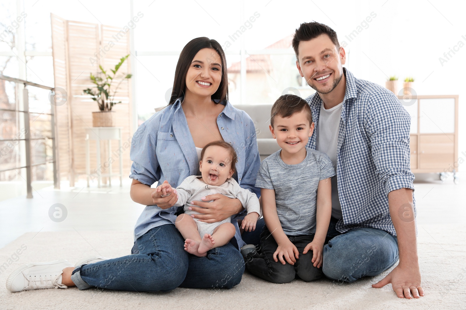 Photo of Happy couple with children sitting on floor at home. Family weekend