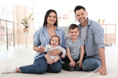 Photo of Happy couple with children sitting on floor at home. Family weekend