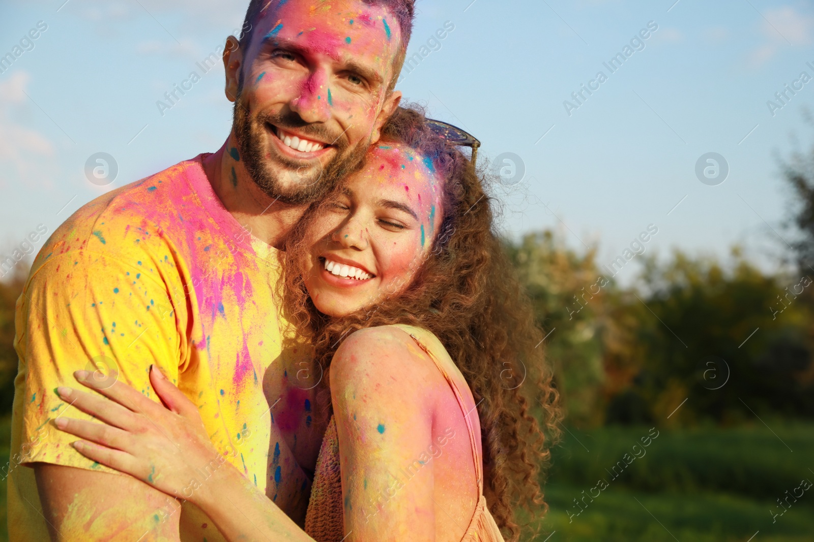 Photo of Happy couple covered with colorful powder dyes outdoors. Holi festival celebration