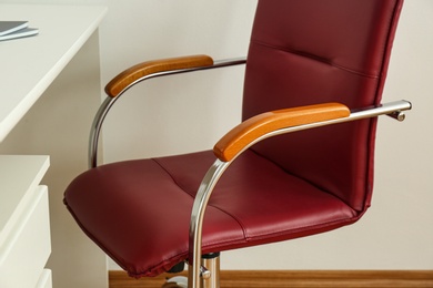 Modern office chair near table indoors, closeup. Stylish workplace interior