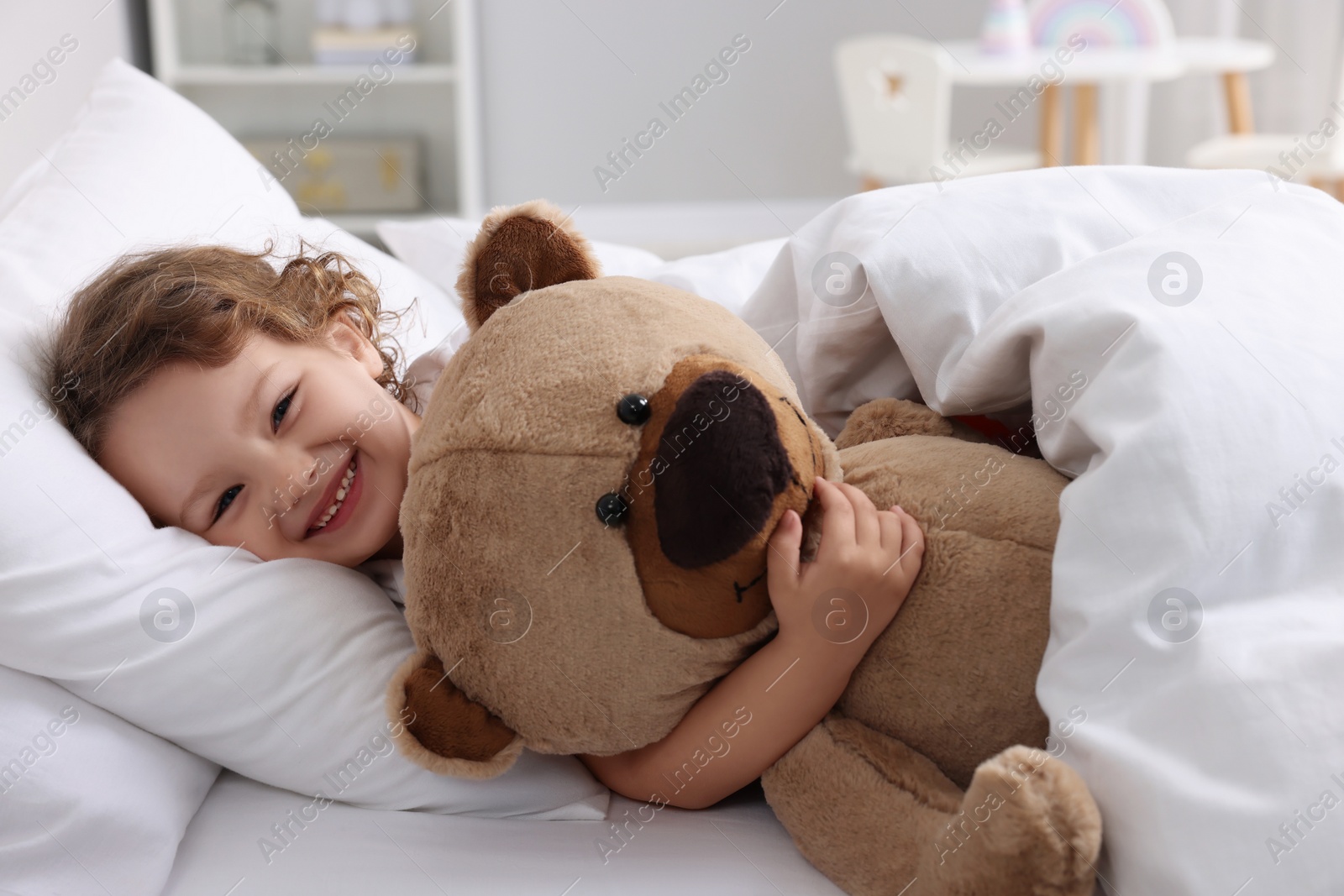 Photo of Cute little girl lying with teddy bear on bed at home