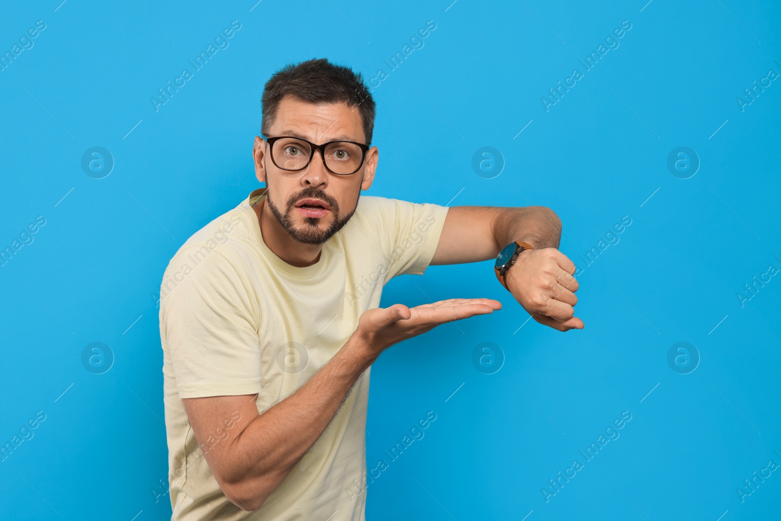 Photo of Man showing time on watch against light blue background. Being late concept