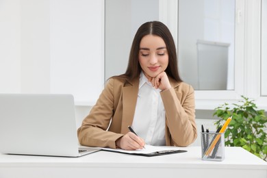 Photo of Young female intern working with laptop at table in office