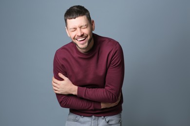 Handsome man laughing on grey background. Funny joke