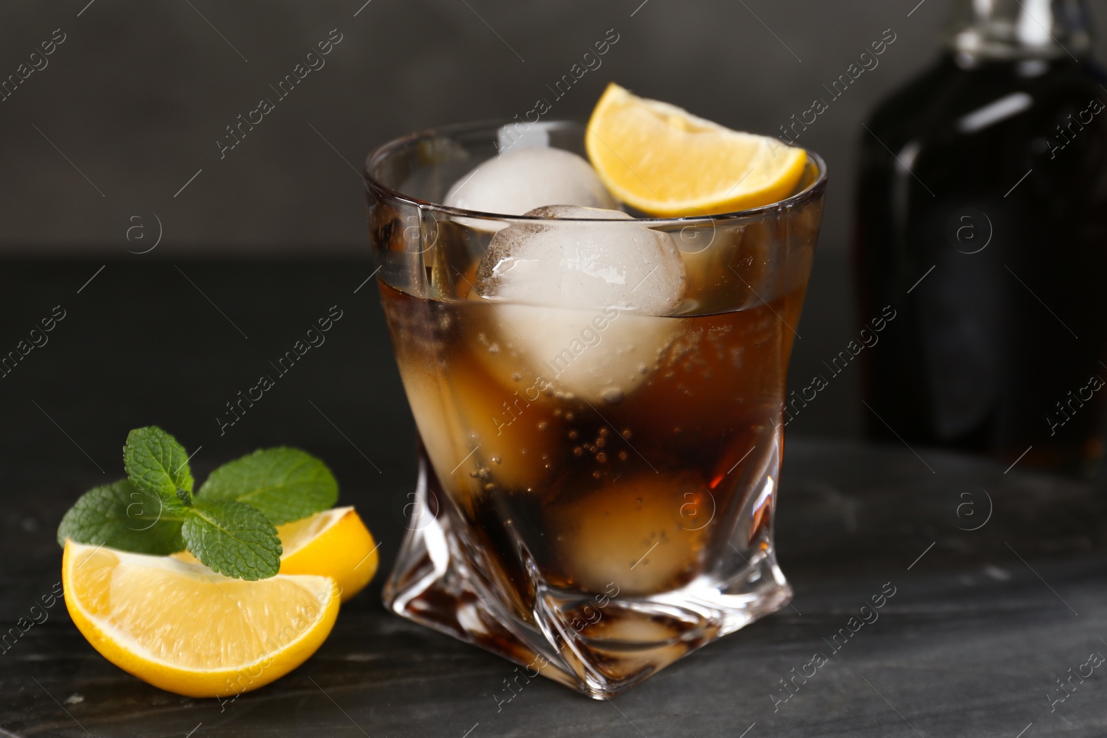 Photo of Delicious cocktail with lemon, ice balls and mint on marble board