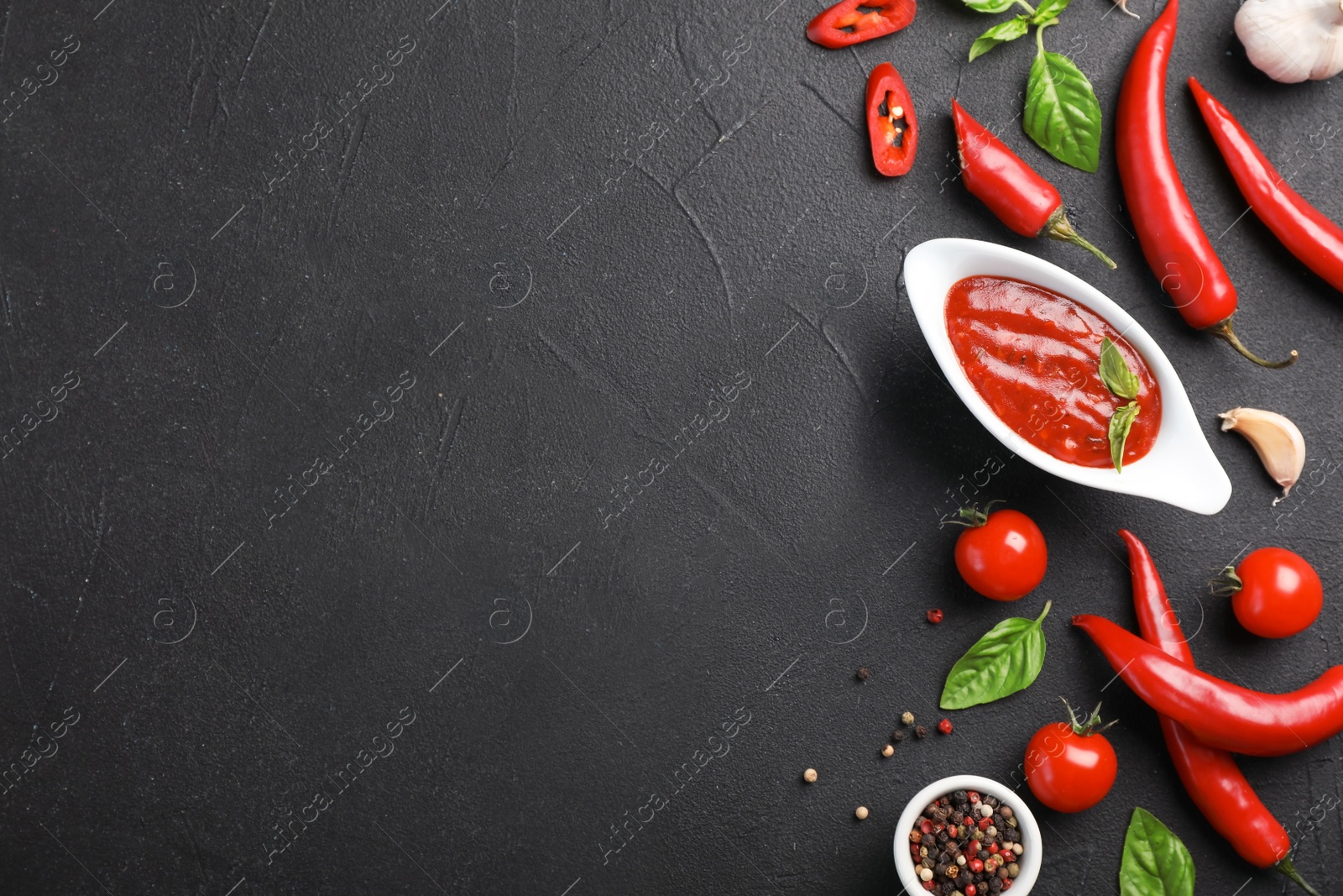 Photo of Flat lay composition with gravy boat of hot chili sauce and different spices on dark background