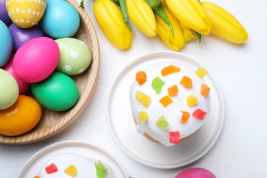 Photo of Easter cakes, color eggs and tulips on white wooden table, flat lay
