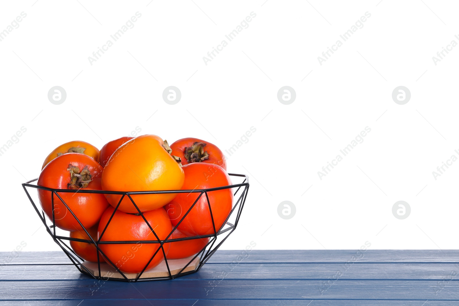 Photo of Delicious ripe juicy persimmons in basket on wooden table against white background