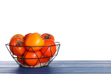 Delicious ripe juicy persimmons in basket on wooden table against white background