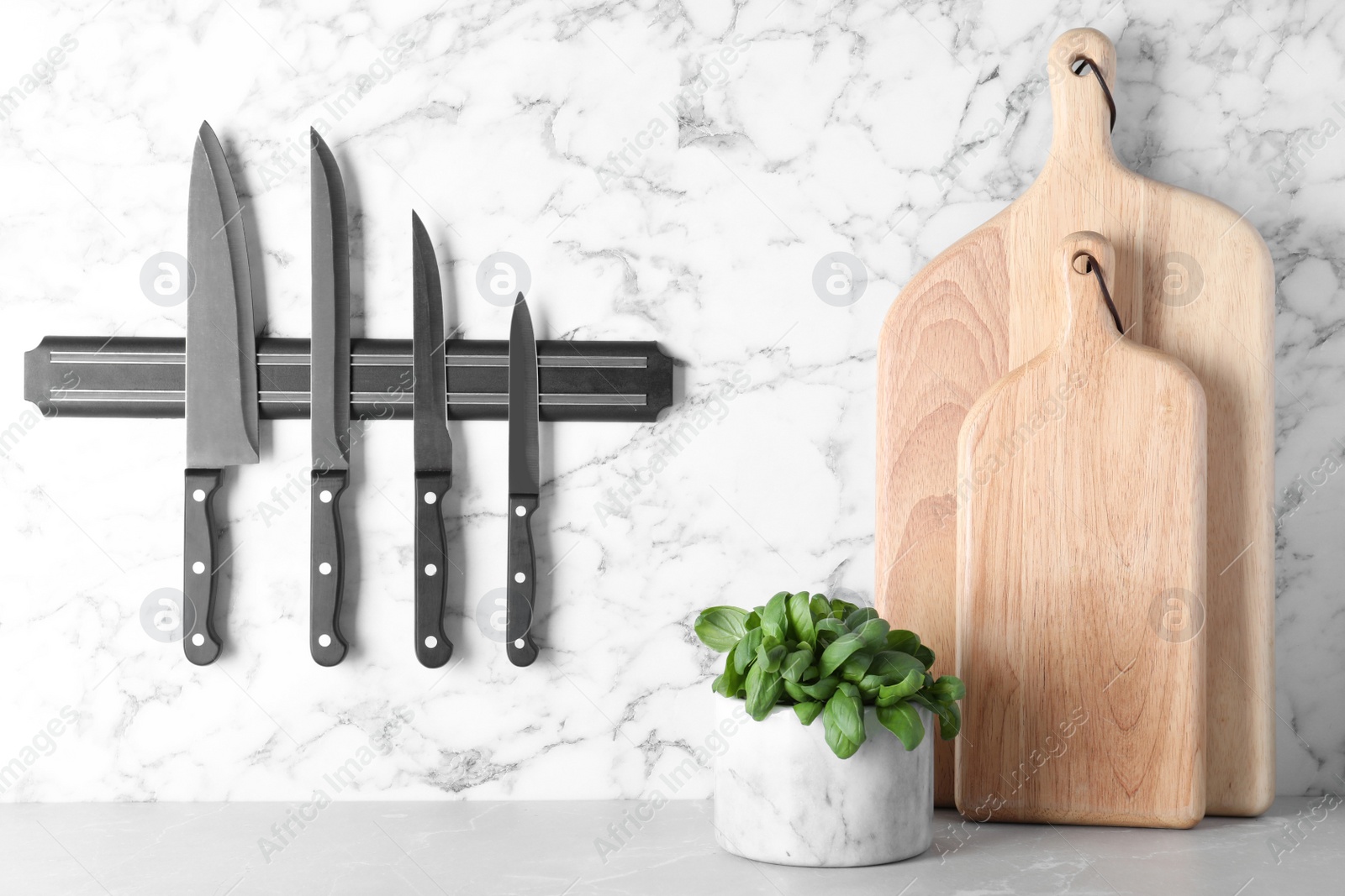Photo of Magnetic holder with set of knives on marble wall in kitchen