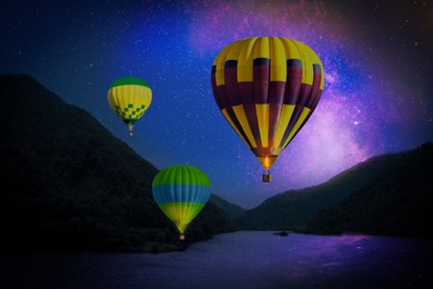 Image of Bright hot air balloons flying over lake at night