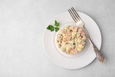 Photo of Tasty Olivier salad with boiled sausage and fork on light table, top view. Space for text