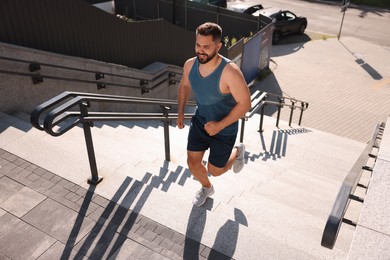 Smiling man running up stairs outdoors on sunny day, above view. Space for text