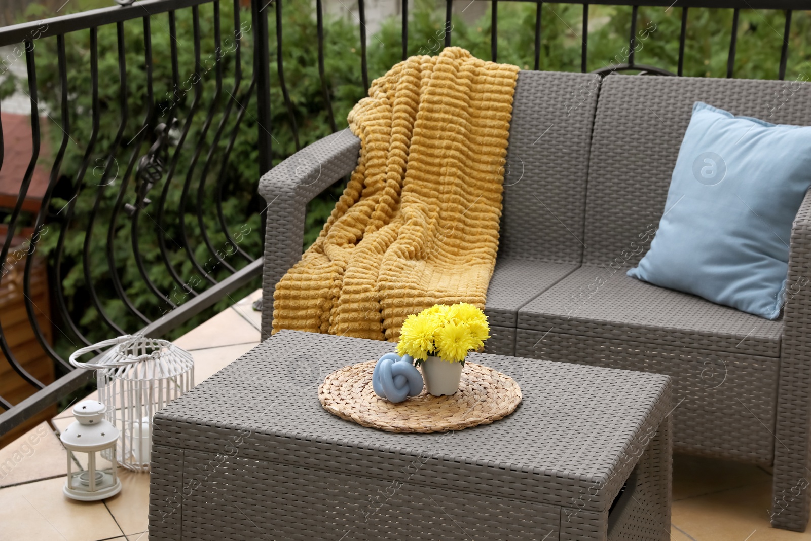 Photo of Light blue pillow, soft blanket and yellow chrysanthemum flowers on rattan garden furniture outdoors