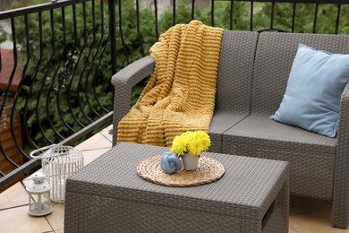 Photo of Light blue pillow, soft blanket and yellow chrysanthemum flowers on rattan garden furniture outdoors