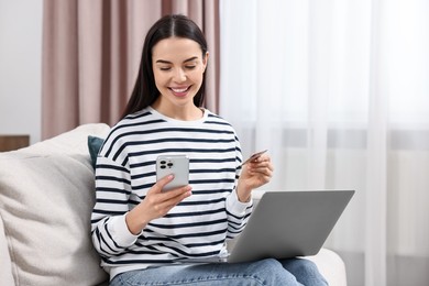 Happy young woman with credit card and gadgets shopping online at home