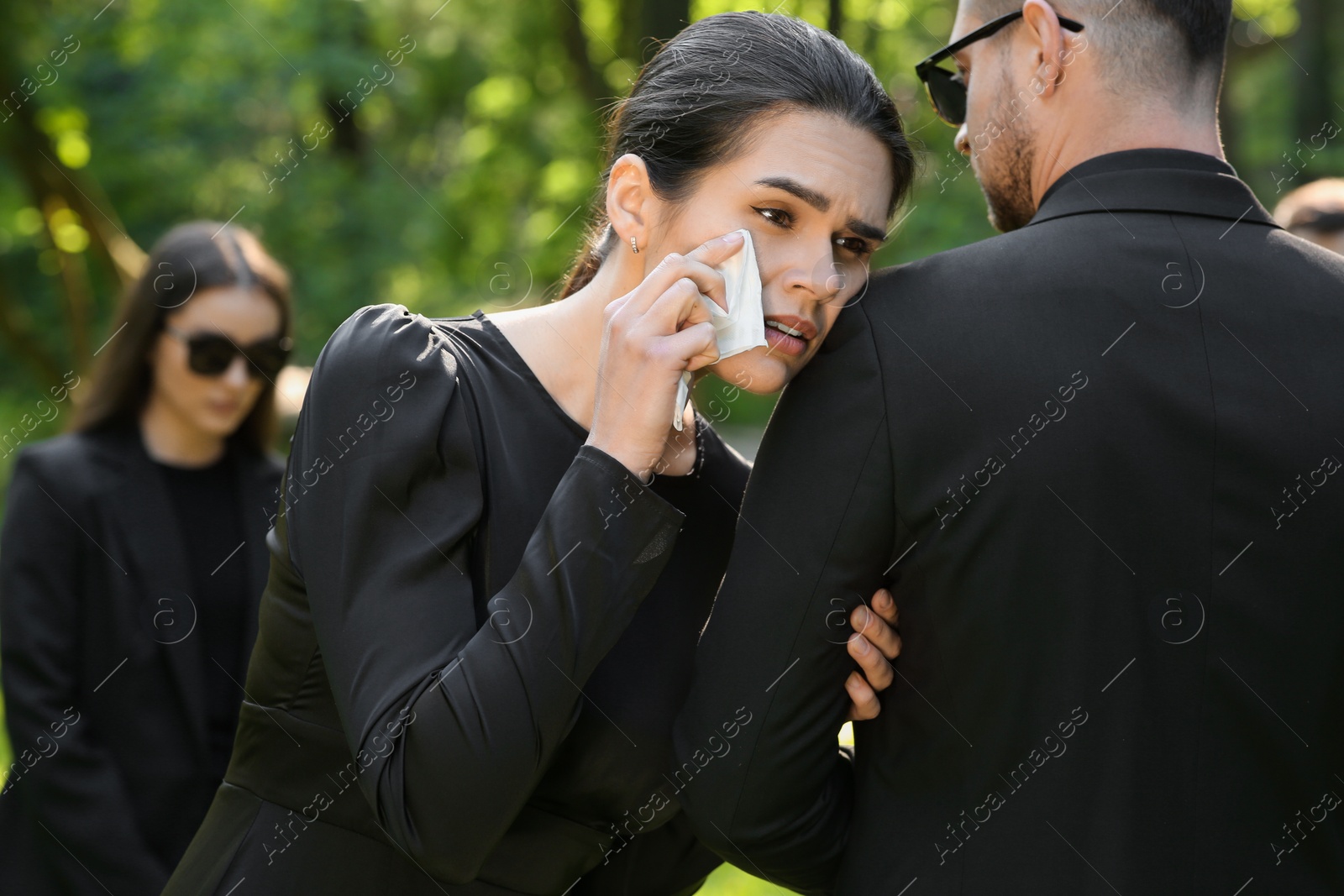 Photo of Sad people in black clothes mourning outdoors. Funeral ceremony