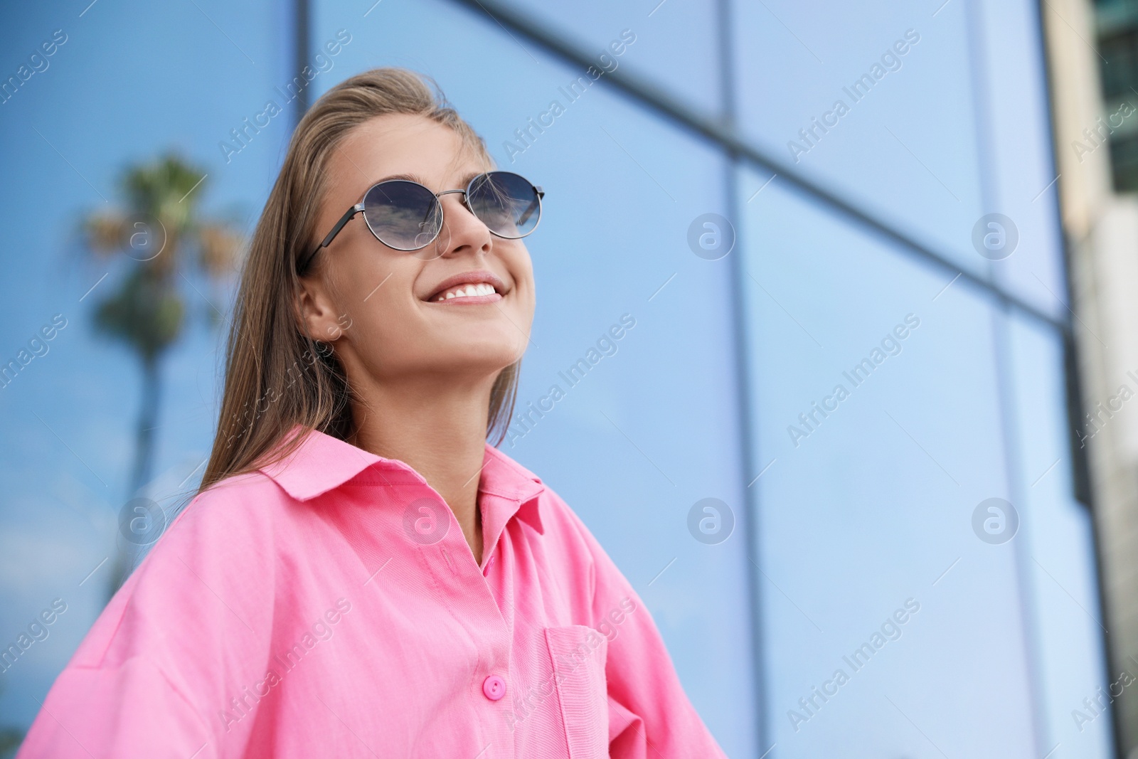 Photo of Portrait of beautiful young woman in stylish sunglasses near building outdoors, space for text