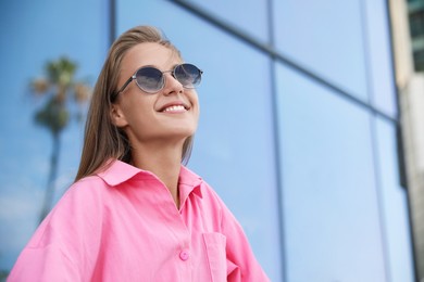 Photo of Portrait of beautiful young woman in stylish sunglasses near building outdoors, space for text