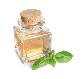 Glass bottle of basil essential oil and leaves on white background