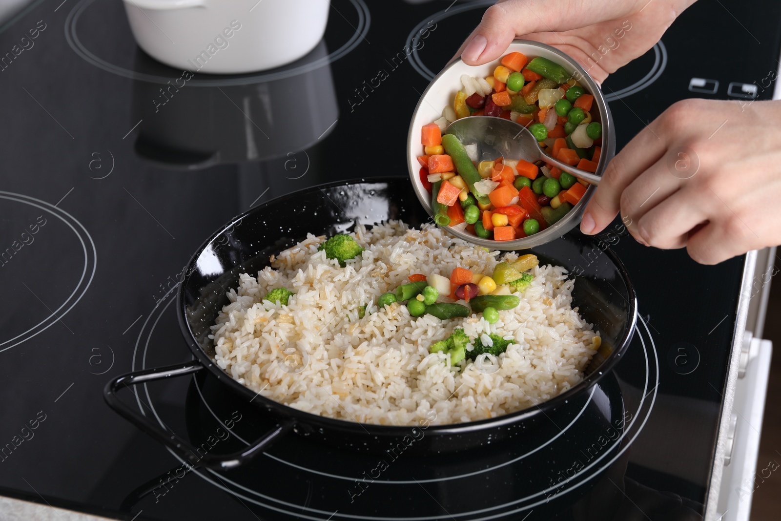 Photo of Woman cooking tasty rice with vegetables on induction stove, closeup