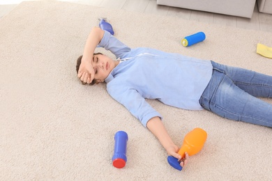 Tired woman lying on carpet surrounded by cleaning supplies