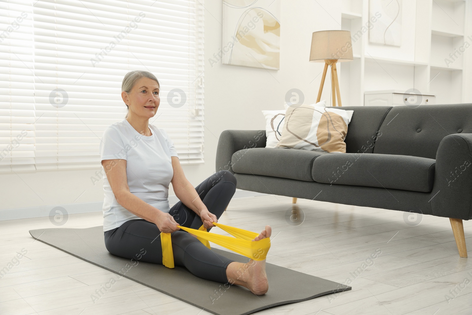 Photo of Senior woman doing exercise with fitness elastic band on mat at home